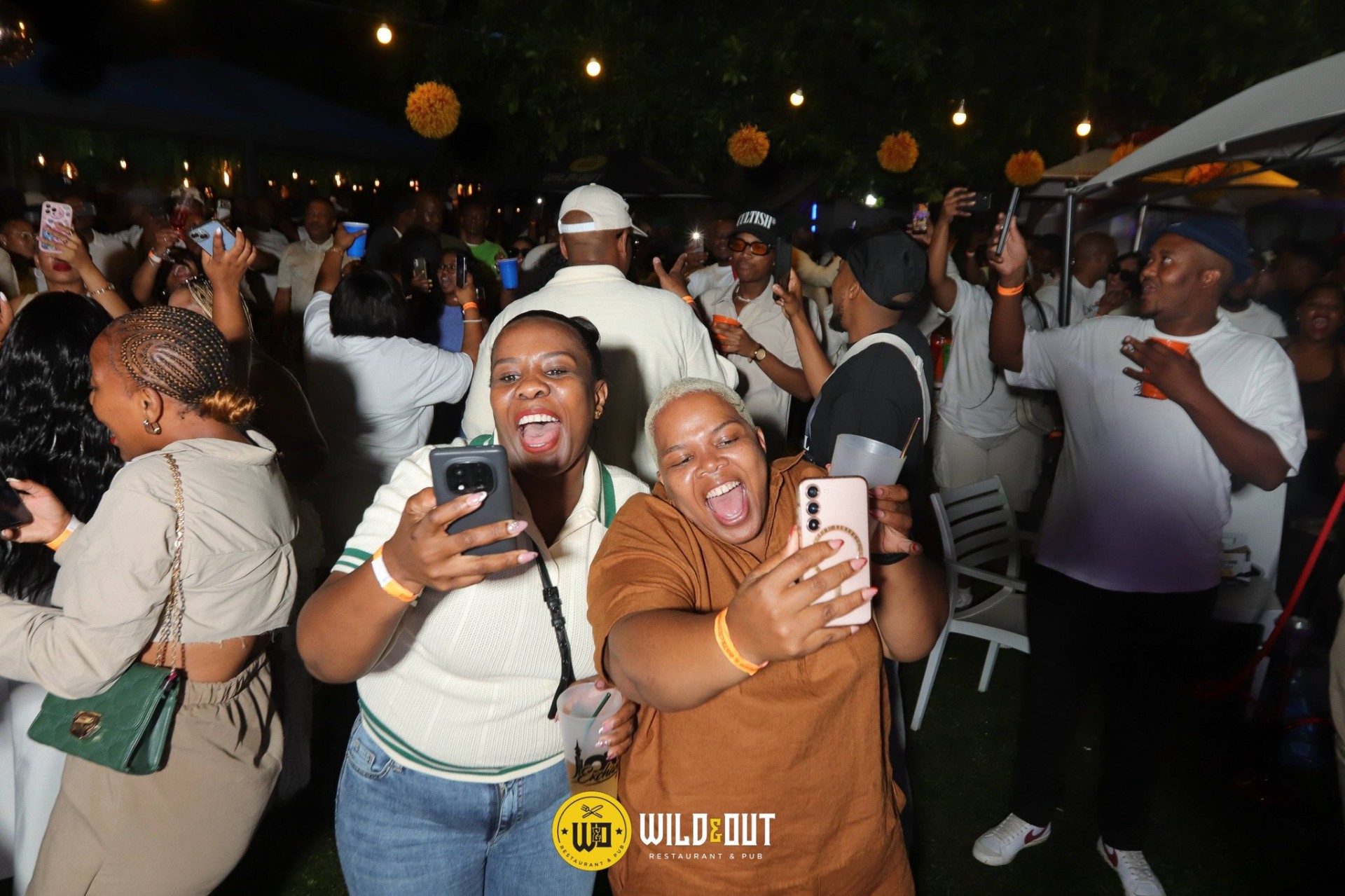 Friends taking selfies at a packed garden party